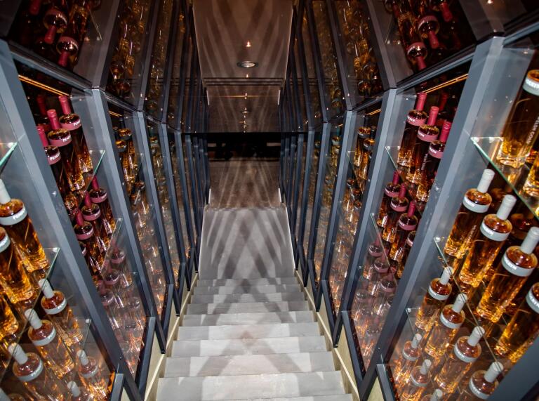 A glass panelled staircase adorned with bottles of whisky leading down to a bar.