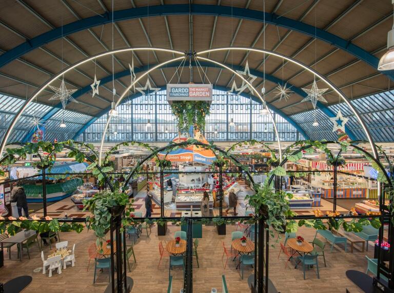 An indoor market with an oval shaped roof framed with lots of glass windows.