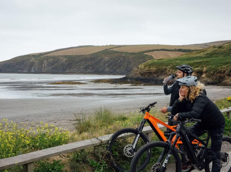 A couple standing next to their bikes looking out at the coast.