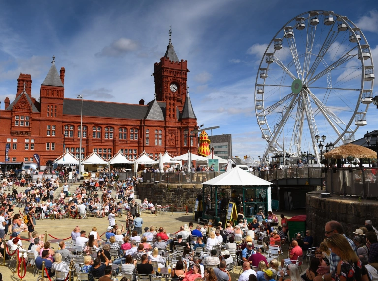 People sitting around a stage, with a big wheel in the background at a food festival.