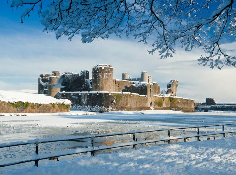 A castle covered with snow surrounded by a frozen moat.