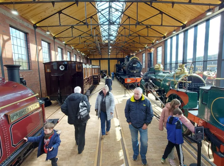 People viewing historic steam locomotives at museum.