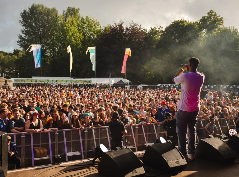 A guy on stage at a festival facing the crowd beyond.