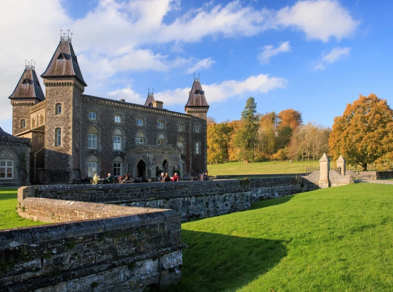 Group of people sitting outside a grand house on a sunny day.