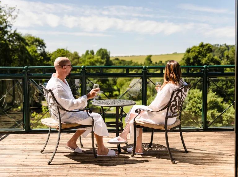 A couple enjoying a glass of wine on their hotel balcony with countryside views