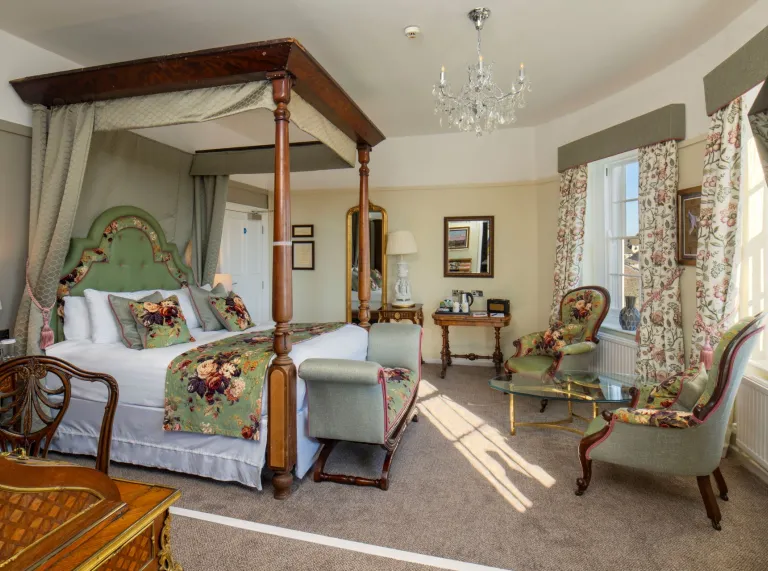 A room in a hotel with a four poster bed and floral furnishings.