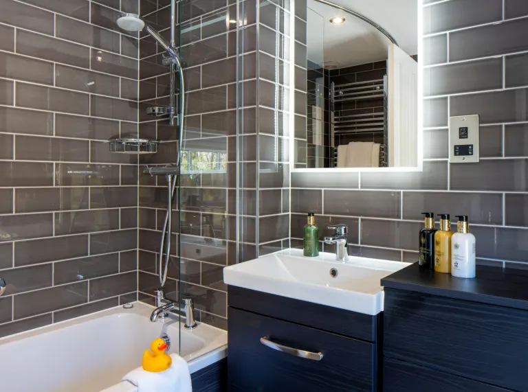 A bathroom in a hotel with a bath and overhead shower.