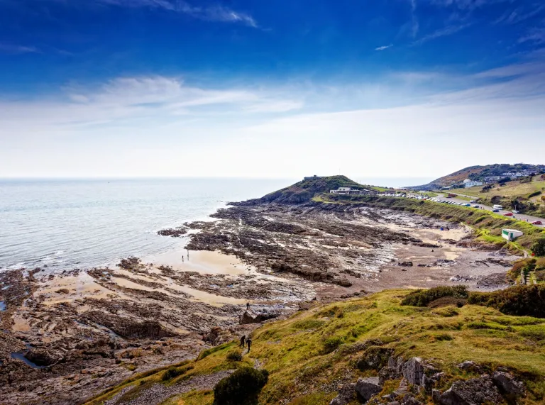 Walkers on a clifftop path with views of the bay beyond.