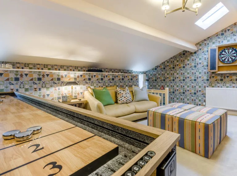 A room in the eaves with a shuffleboard, dartboard and sofas.