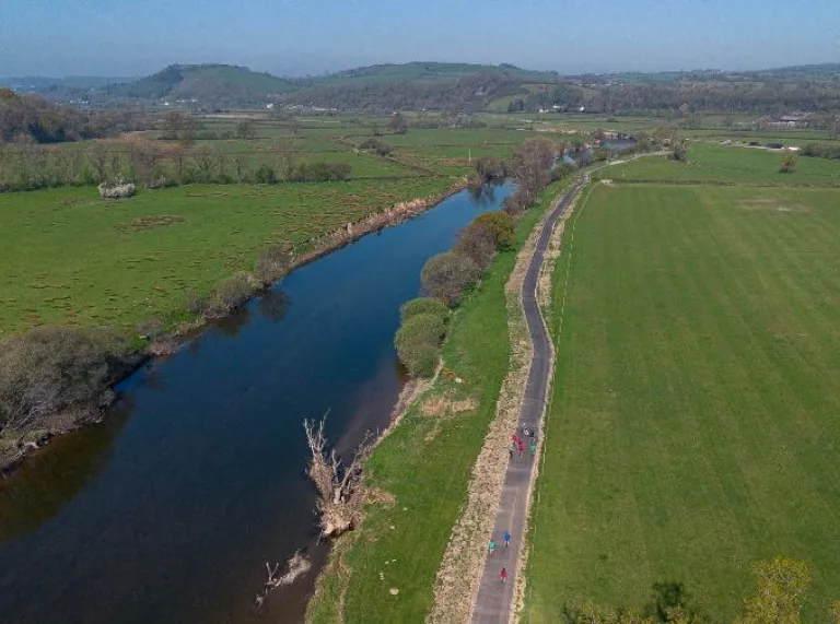 Aerial shot of a walking path in the countryside running alongside a river.