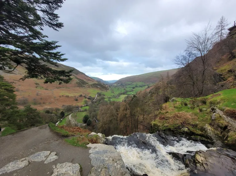 A waterfall leading down to a river next to a walking path.