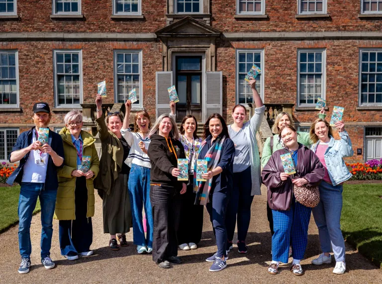 A group of people outside an grand estate holding visitor attraction leaflets.
