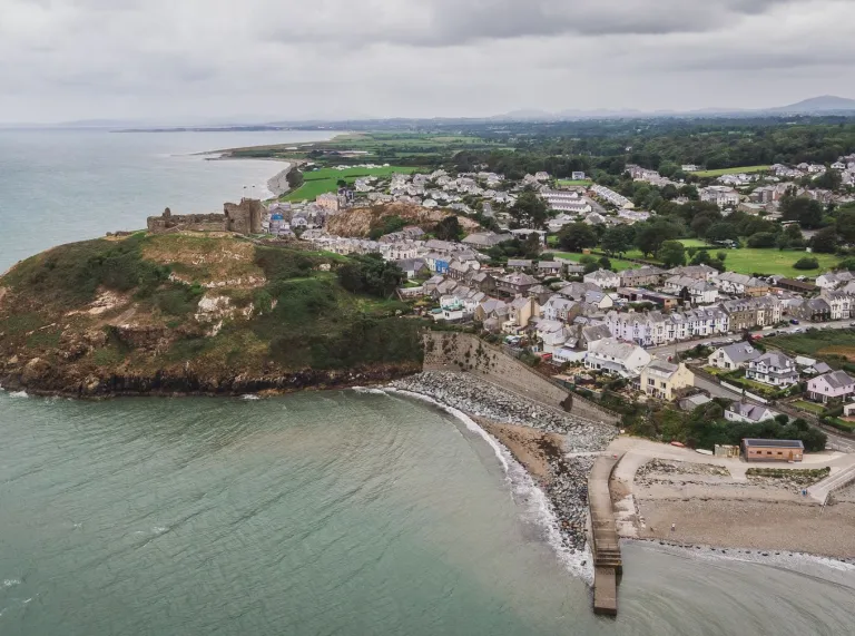Aerial shot of a castle on a clifftop, by a beach and town.