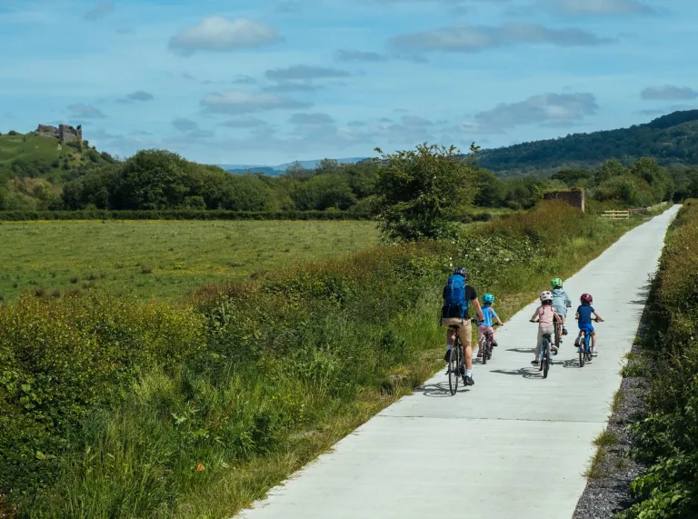Family of cyclists on a path with castle ruins in the foreground.