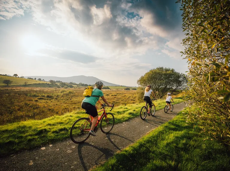 A family cycling along a path with mountains in the distance.
