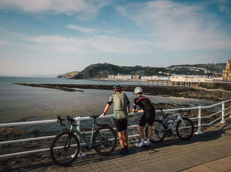 Cyclists parked up on a promenade looking out over a coastline.