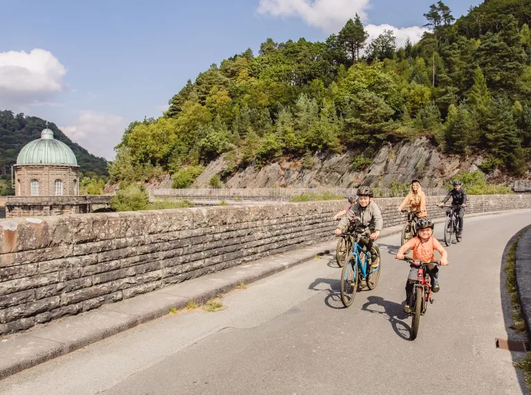 Family of cyclists crossing a bridge across a dam.
