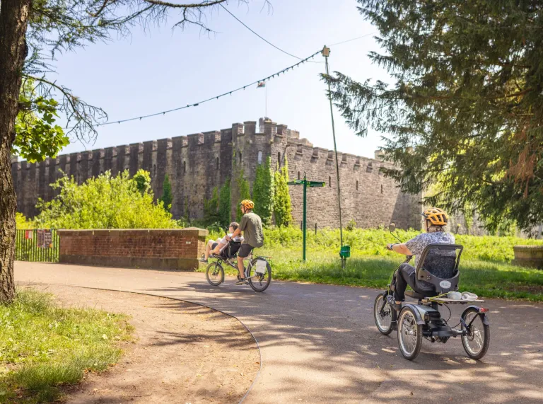 Adaptable bikes going past a castle in a park.