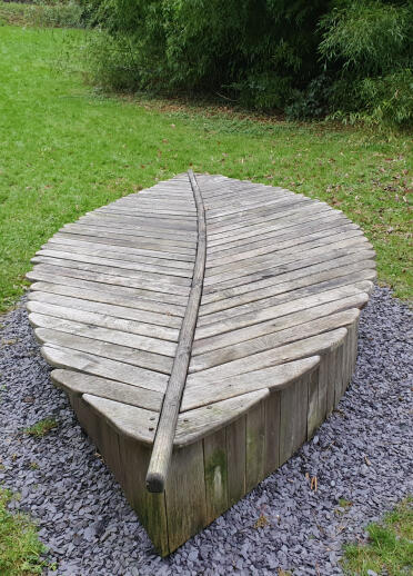 A wooden medieval chair shaped like a leaf on a walking trail .