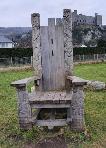A medieval wooden chair on grass with a castle in the background.