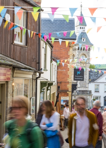 People walking around a book town with a clock tower in the background.