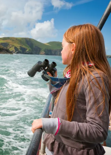 Girl on a boat trip holding binoculars looking out to sea near New Quay.