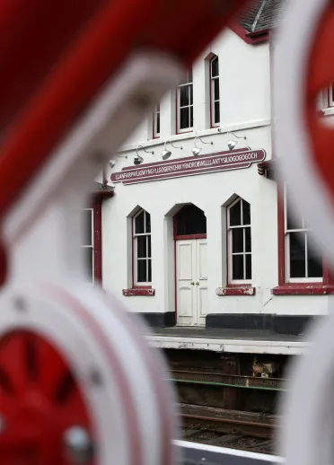 A shot of Llanfair PG sign through the colourful railings of the bridge crossing.