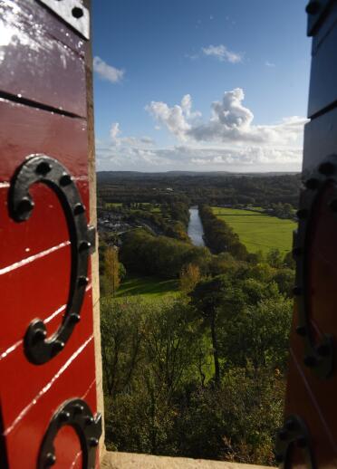 Views of a river and fields framed by the castle window with red shutter.