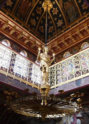 An ornate ceiling and fixture depicting a golden statue in a castle.