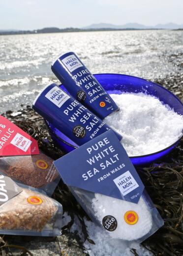 A range of Halen Môn sea salt products displayed on the coast against the tide.