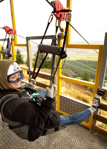 Two people at the top of a seated zip line ready to launch.