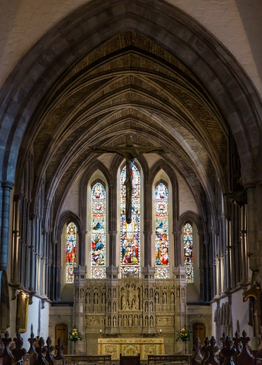 Interior of an arch in a cathedral leading to an altar and large stained glass window.