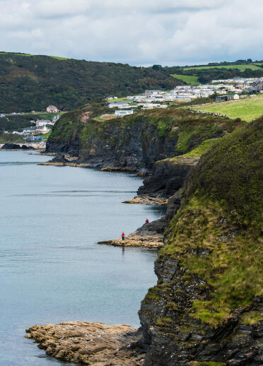 People walking above the cliffs on the Ceredigion coastline at Tresaith, with caravans in the background.