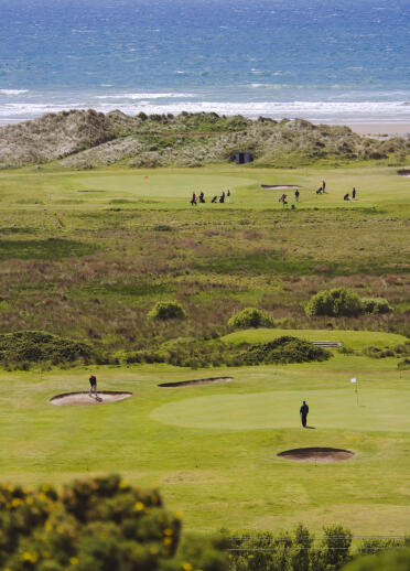 Golfers playing on different holes with seascape views at Aberdovey Golf Club.