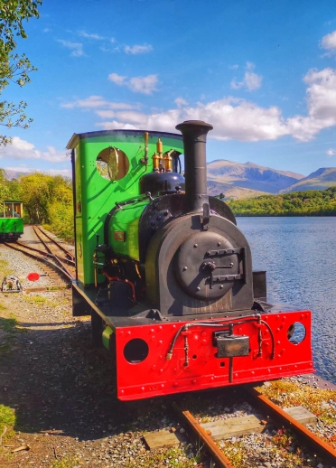 A steam train travelling past a lake and mountains.