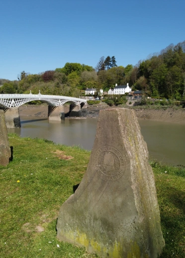 Stones marking Offa's Dyke Path by a river and iron bridge.