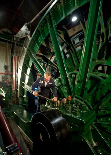 A volunteer working on the wheel of a large engine in a museum.