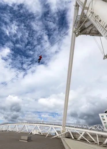A person ziplining above the roof of a sports stadium.