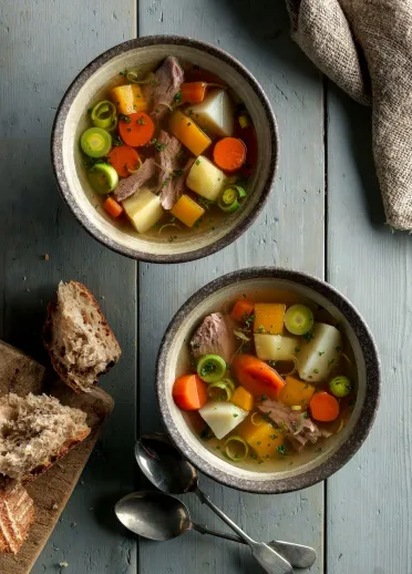 A bowl of stew with meat and vegetables, served with crusty bread.