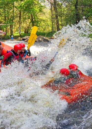 A group of people in a raft crashing through rapids on a river.