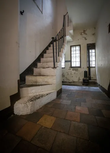 A jail with a white stone staircase in a hallway with peeling paint on the walls.