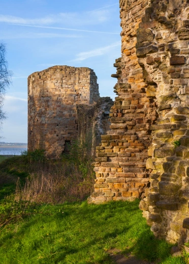 The ruins of a castle on a grassy bank with views of the coast beyond.