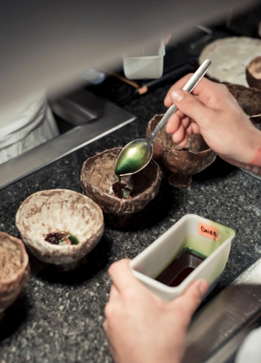 A chef spooning onion oil over food presented in bowls.