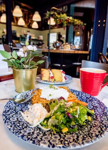 A plate of Welsh rarebit served with salad and coleslaw along with cake and drink.