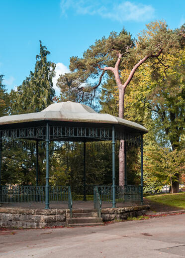 A bandstand in a park with a castle beyond the trees and parkland.