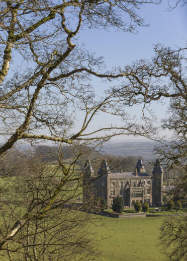 View of Newton House in the distance at Dinefwr, with trees in the foreground.