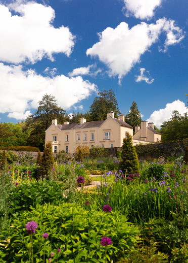 Aberglasney garden displaying flowers and shrubs with manor house in background.