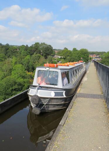 A narrowboat travelling along an aqueduct on a sunny day.