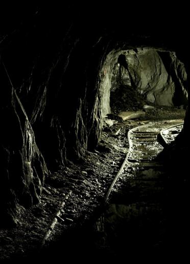 A mine cart track inside a mine looking toward the exit.