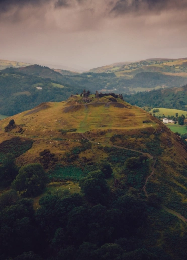 Ruins of a castle on a hill with mountains and countryside beyond.
